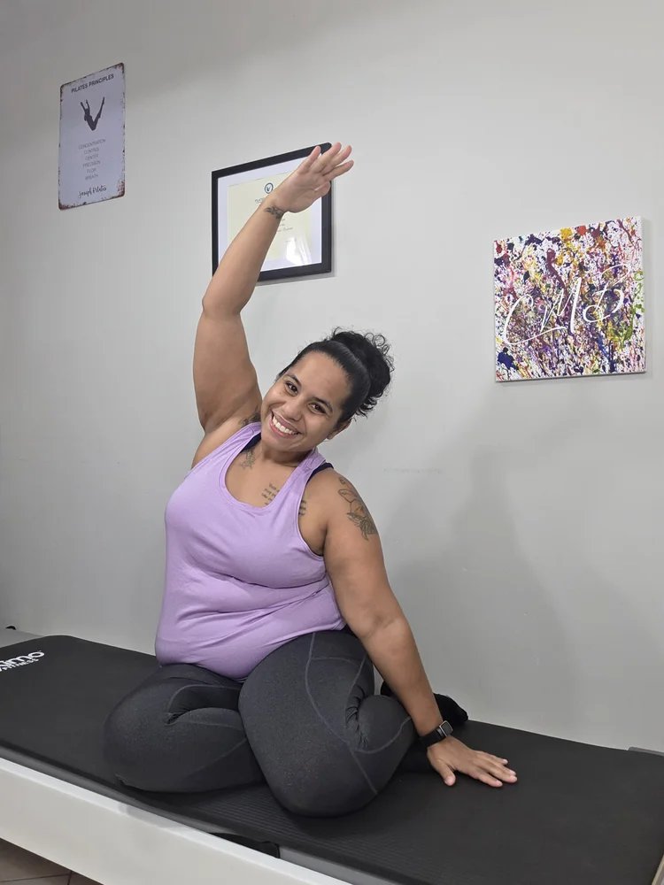 Christine of CMB Pilates demonstrating a seated side stretch on a Pilates mat