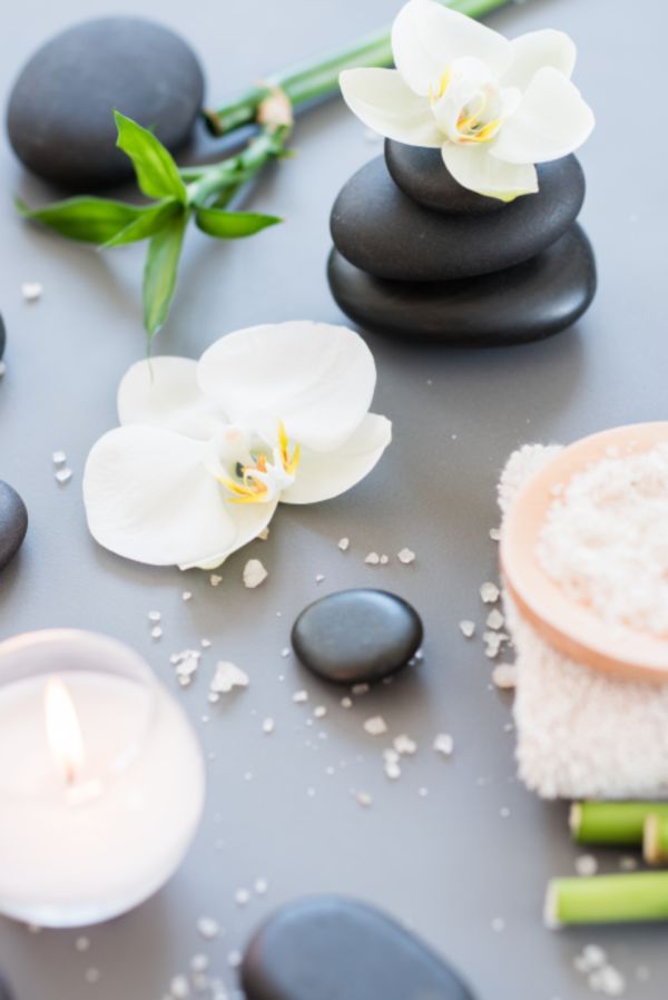 Spa flatlay with warm stones, orchids, candle, bath salts and bamboo