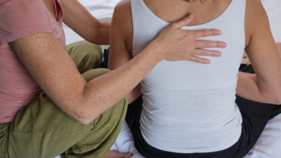 Practitioner's hand resting gently on a seated client's upper back during a somatic healing session in Wyomissing
